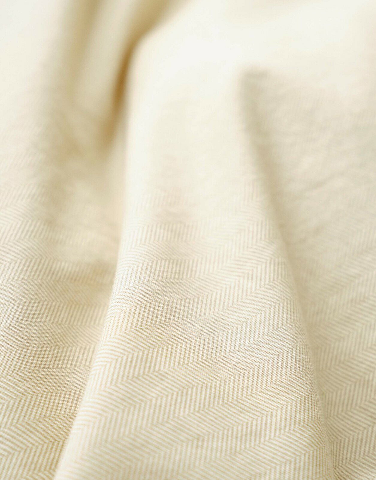 Nahaufnahme einer cremefarbenen Bettwäsche mit dezentem Fischgrätenmuster, aus seitlicher Perspektive fotografiert.
