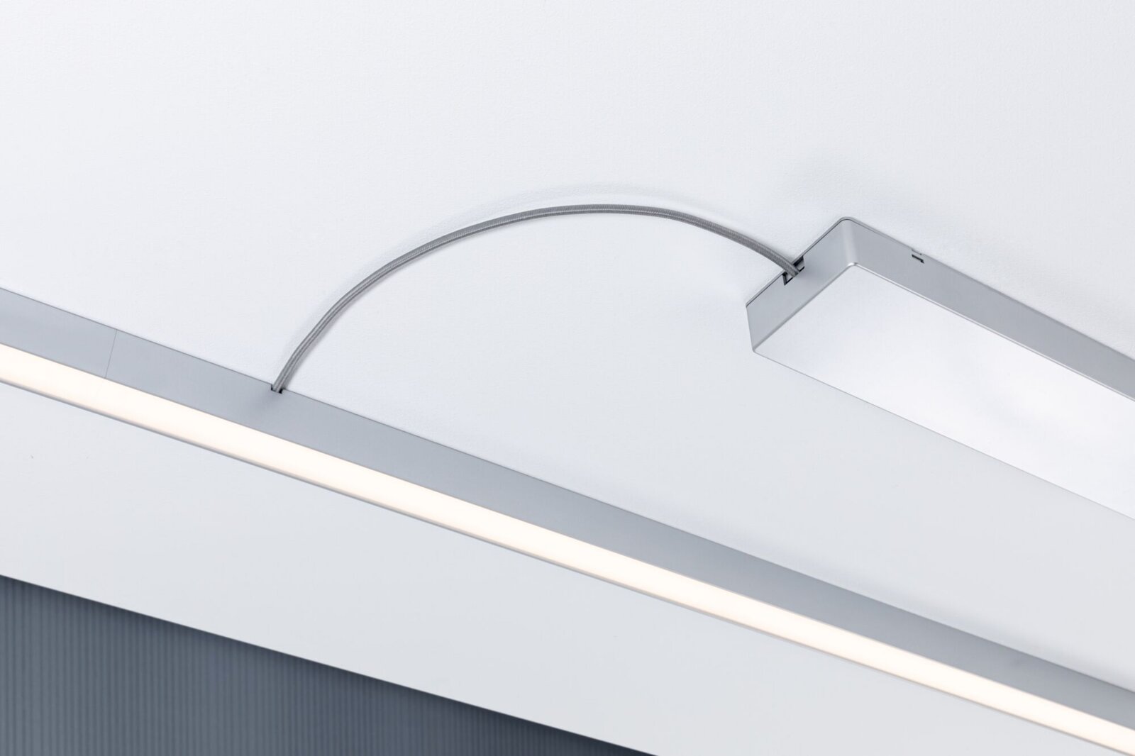 Moderne, schlanke LED-Deckenleuchte in Silber mit linearem Lichtband und gebogenem Anschlusskabel, fotografiert aus der Untersicht schräg von unten