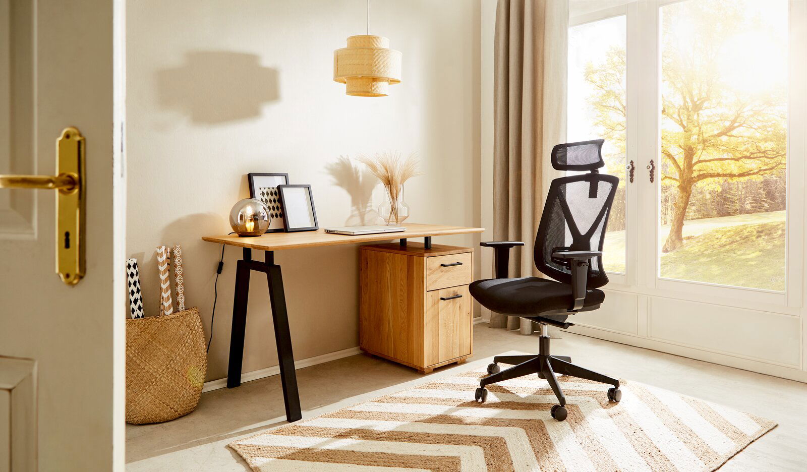 Moderner Schreibtisch mit Holzplatte und schwarzen Metallbeinen, seitlich von einem ergonomischen Bürostuhl und einem Fenster mit Blick auf einen sonnigen Garten.