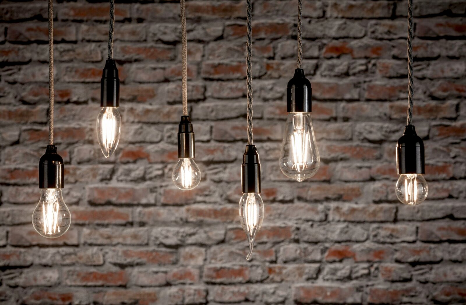 Mehrere hängende LED-Leuchtmittel vor einer Ziegelwand, seitliche Perspektive.