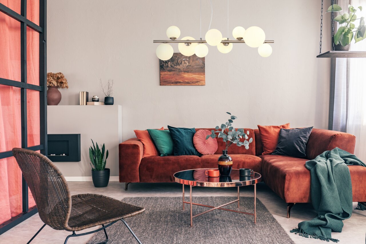 Moderne Hängeleuchte mit mehreren kugelförmigen Lampen, zentral über einem stilvoll eingerichteten Wohnzimmer mit rotem Sofa und Couchtisch, aus der Perspektive des Raumes betrachtet.