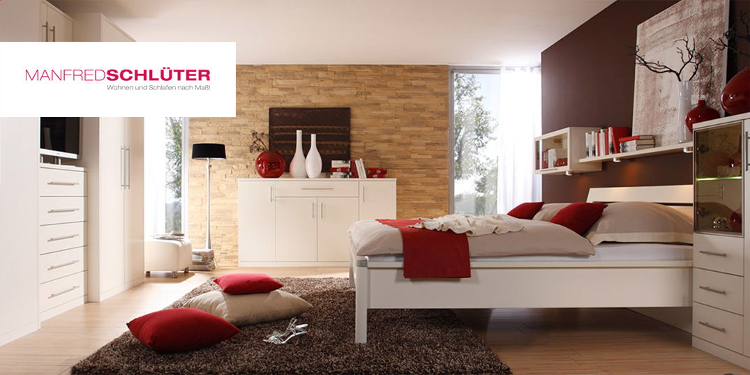 Logo MANFRED SCHLÜTER Schlafzimmer mit weißen Möbeln, dekoriert mit roten Elementen.