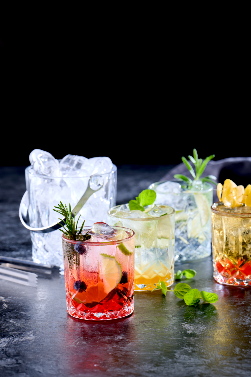 Eiskübel mit Eiswürfeln und vier Gläser mit verschiedenen Getränken, von vorne fotografiert.