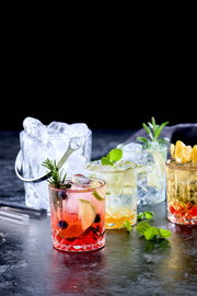 Eiskübel mit Eiswürfeln und vier Gläser mit verschiedenen Getränken, von vorne fotografiert.