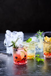 Eiskübel mit Eiswürfeln und vier Gläser mit verschiedenen Getränken, von vorne fotografiert.