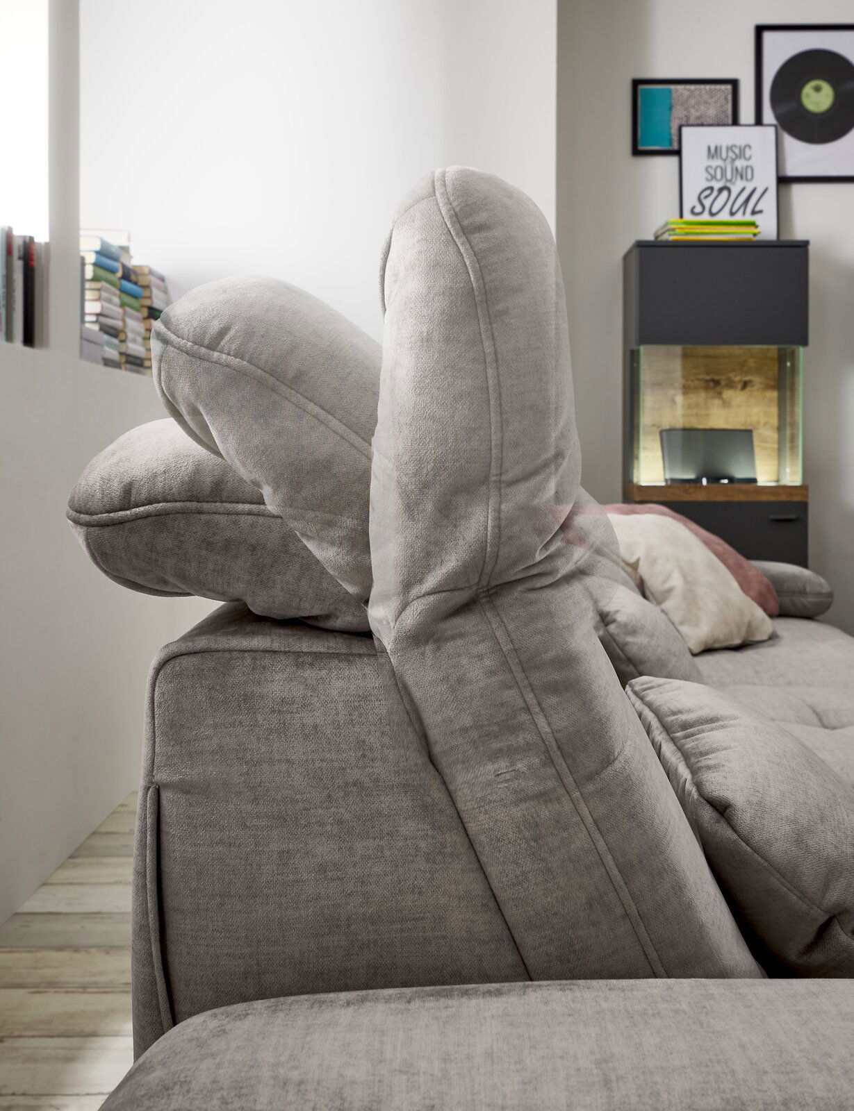 Seitenansicht einer grauen Rundecke mit verstellbaren Kopfstützen in einem modernen Wohnzimmer.