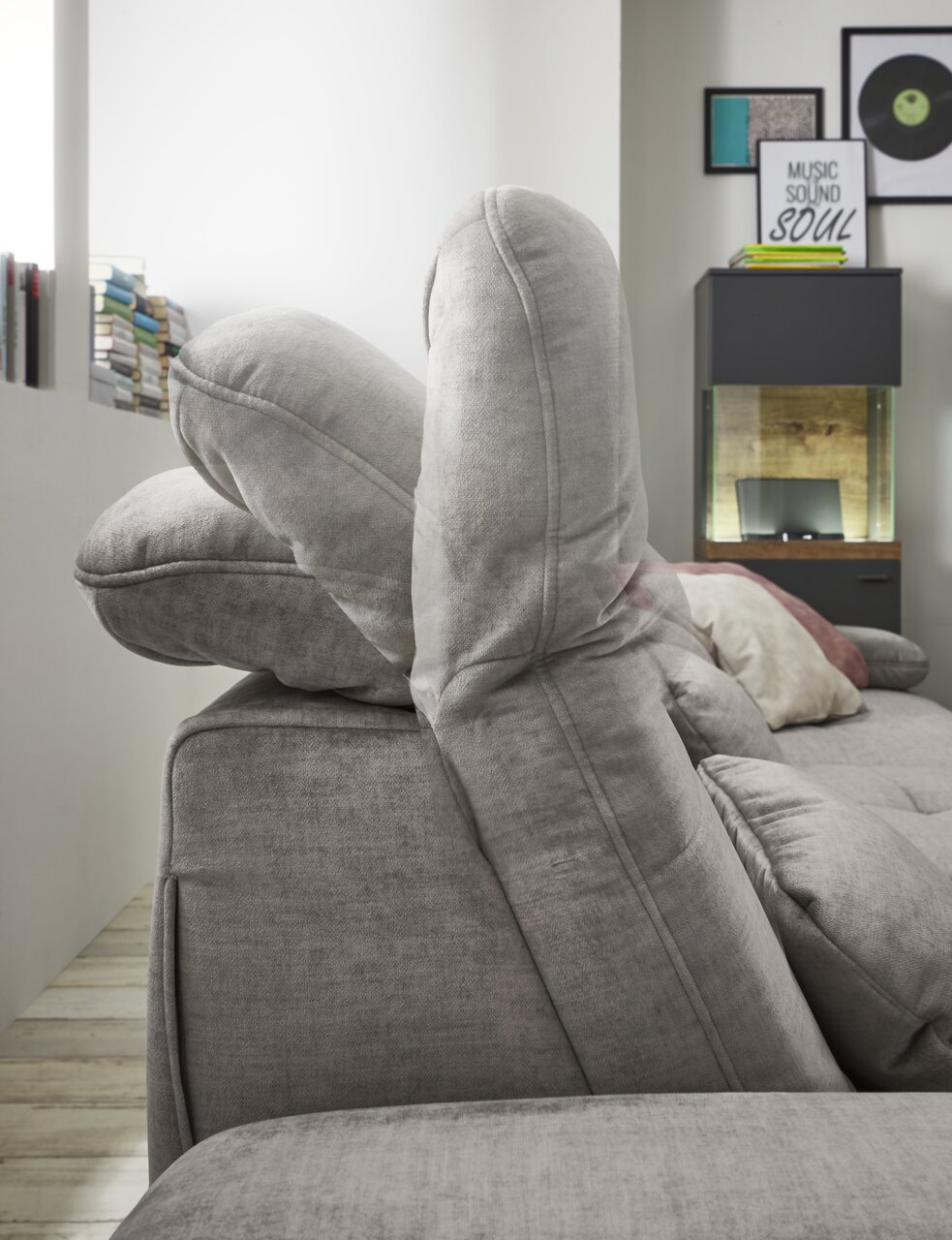 Seitenansicht einer grauen Rundecke mit verstellbaren Kopfstützen in einem modernen Wohnzimmer.
