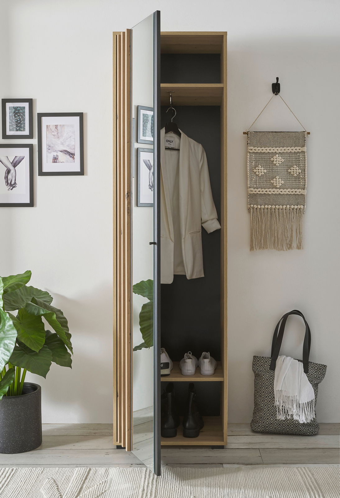 Garderobenschrank mit Spiegel, teilweise geöffnet, zeigt Innenraum mit aufgehängtem Mantel und Schuhen, aus seitlicher Perspektive fotografiert.