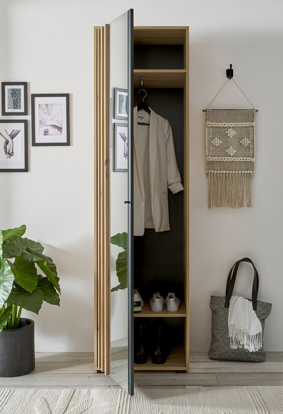 Garderobenschrank mit Spiegel, teilweise geöffnet, zeigt Innenraum mit aufgehängtem Mantel und Schuhen, aus seitlicher Perspektive fotografiert.