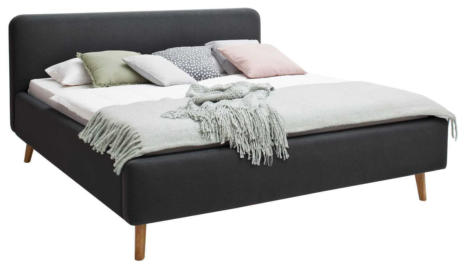 Polsterbett in Dunkelgrau mit Holzfüßen, dekoriert mit mehreren Kissen und einer Decke, seitliche Perspektive