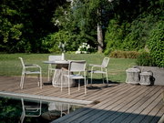 Moderner Stapelsessel auf einer Terrasse neben einem runden Tisch, umgeben von einem grünen Garten, aus der Perspektive von schräg vorne.