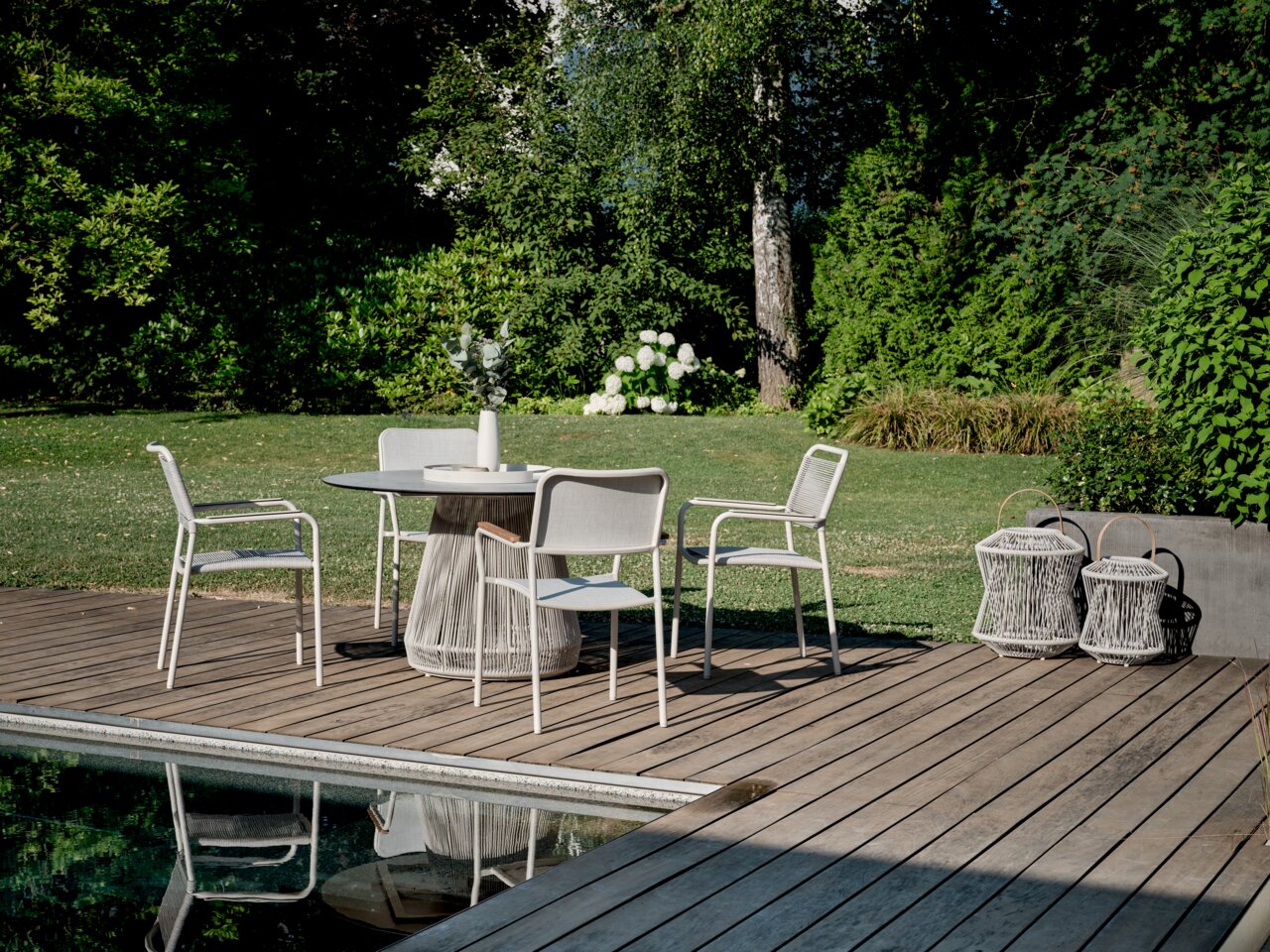 Moderner Stapelsessel auf einer Terrasse neben einem runden Tisch, umgeben von einem grünen Garten, aus der Perspektive von schräg vorne.
