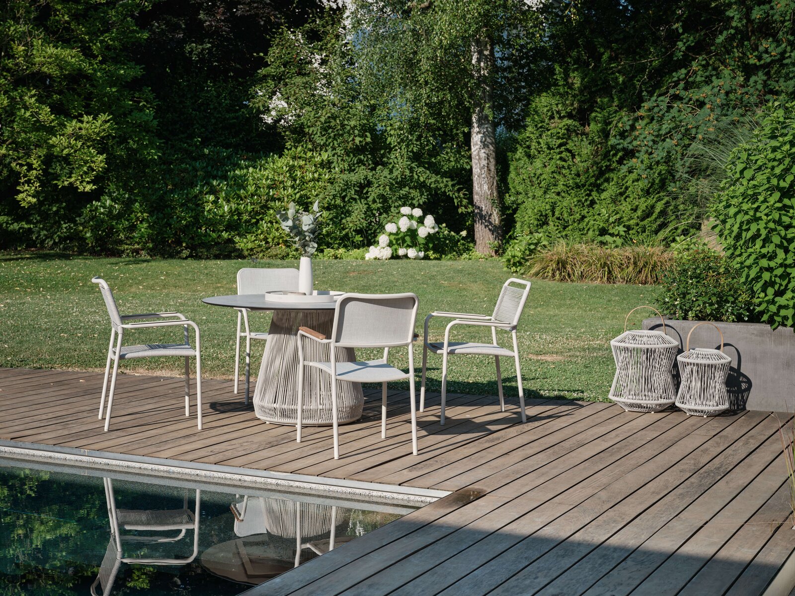 Moderner Stapelsessel auf einer Terrasse neben einem runden Tisch, umgeben von einem grünen Garten, aus der Perspektive von schräg vorne.