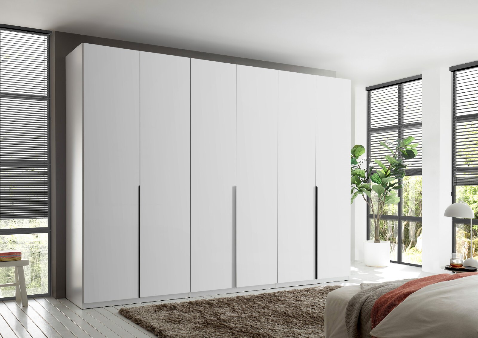 Großer weißer Kleiderschrank mit sechs grifflosen Drehtüren und drei langen schwarzen Griffleisten, aus leicht seitlicher Frontalperspektive in einem hellen modernen Schlafzimmer gezeigt.