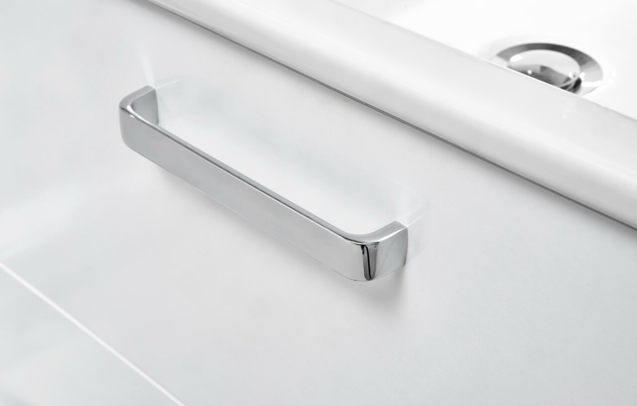 Close-up van een moderne, witte wastafelonderkast met een glanzende, verchroomde handgreep.