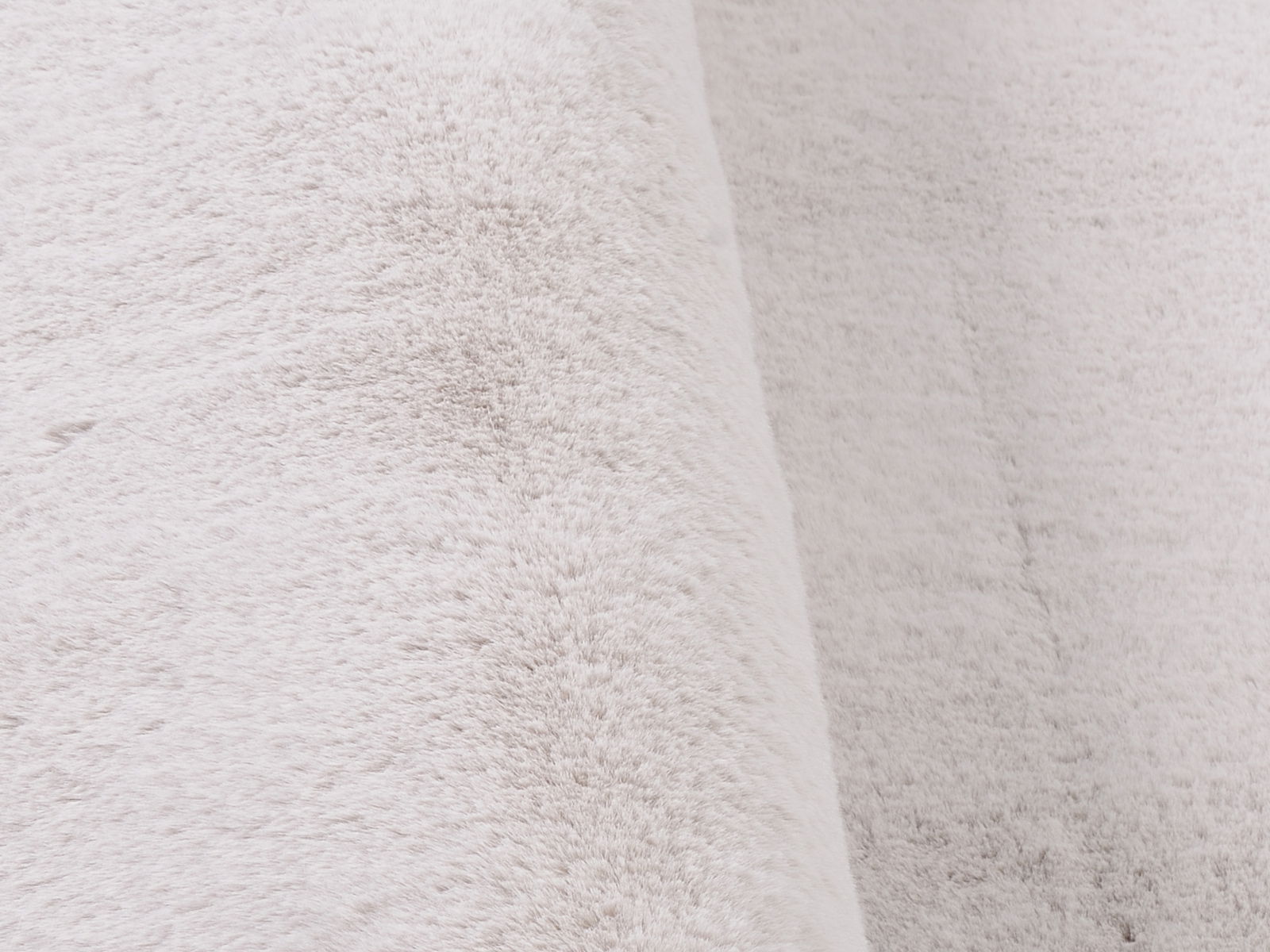 Nahaufnahme eines weichen, weißen Fellteppichs mit flauschiger Textur, seitliche Perspektive