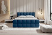 Modernes Polsterbett in tiefblauem Stoff mit gepolstertem, quadratisch gestepptem Kopf- und Fußteil, weißer Matratze und Kissen in hellem Schlafzimmer; Frontalansicht aus Augenhöhe.