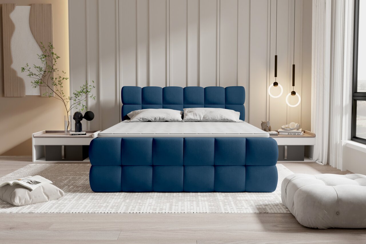 Modern gestoffeerd bed in diepblauwe stof met een gestoffeerd, vierkant doorgestikt hoofdeinde en voeteneinde, een wit matras en kussens in een lichte slaapkamer; vooraanzicht vanaf ooghoogte.