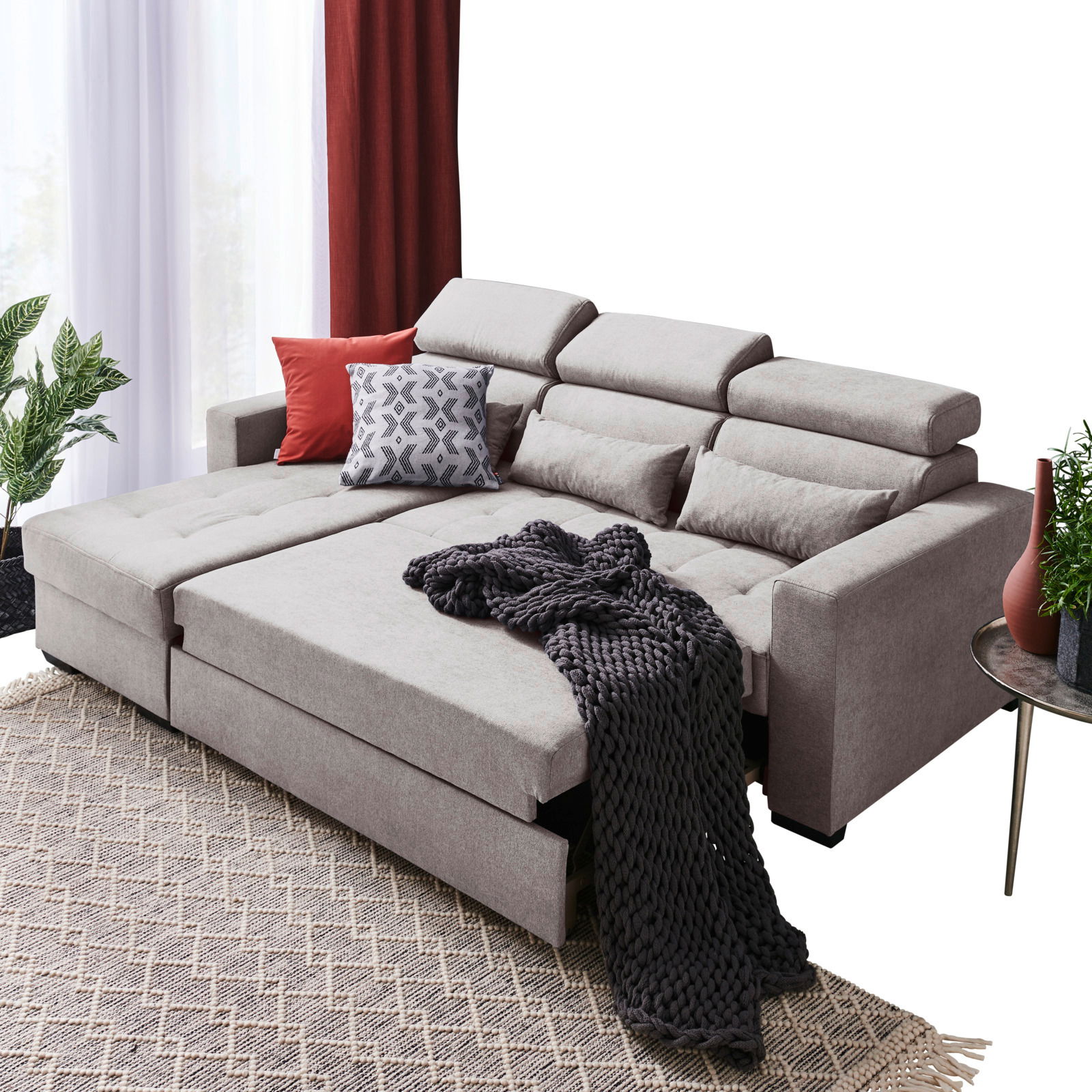 Gemütliche Rundecke in hellem Grau mit verstellbaren Kopfstützen, dekoriert mit Kissen und einer dunklen Decke, aus der Perspektive von vorne links betrachtet.