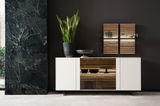 Modernes Sideboard in Weiß mit Glaselementen, dekoriert mit einer Pflanze und einer Schale, vor einer dunklen Wand. Frontalansicht.