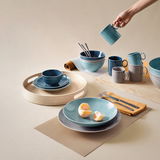 Kaffee-Obertasse in Dunkelblau auf einem gedeckten Tisch, von oben fotografiert, umgeben von Geschirr in verschiedenen Blautönen.