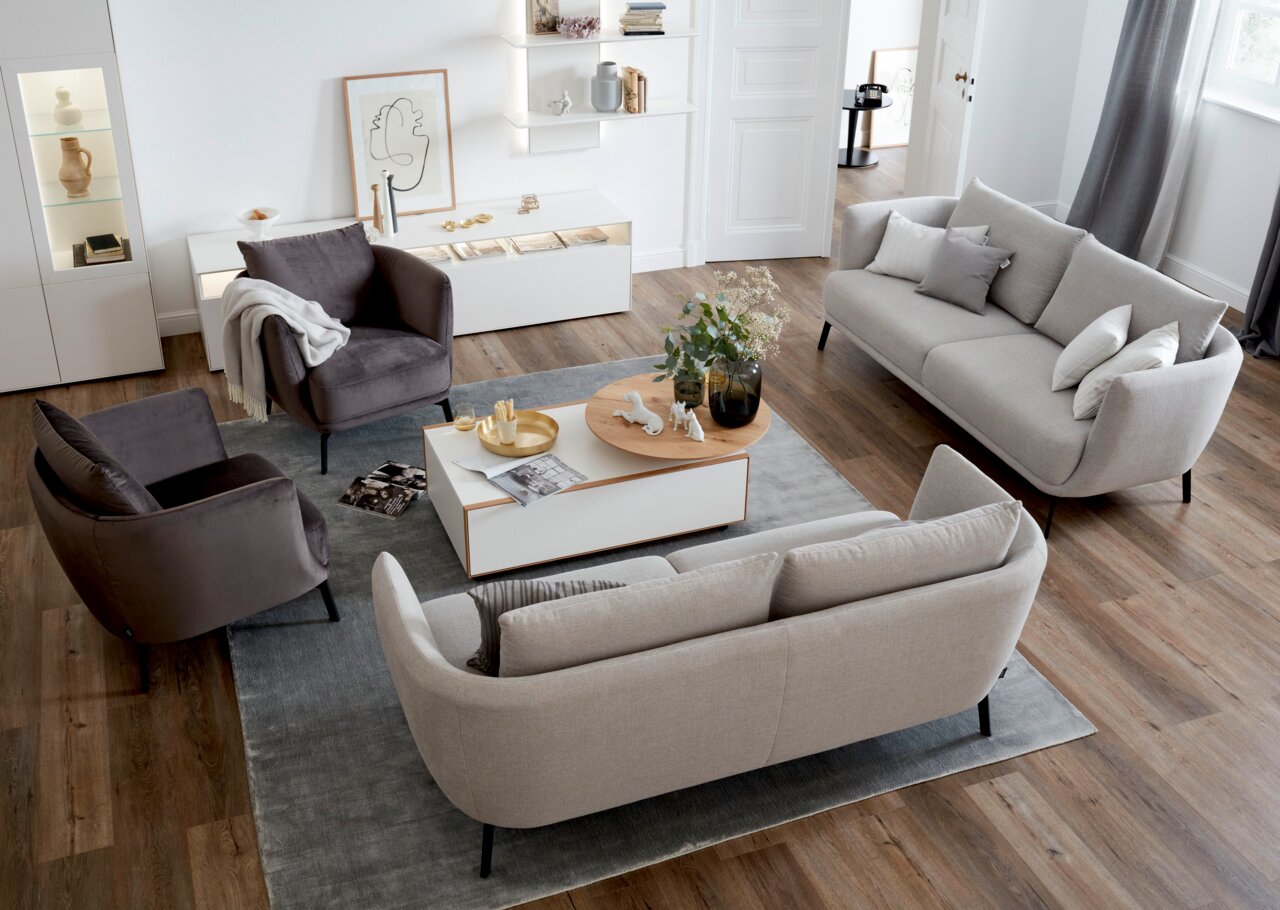 Wohnzimmer mit modernem Sessel in dunklem Stoff, umgeben von einem hellen Sofa und einem Couchtisch, aus der Vogelperspektive betrachtet.