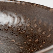 Nahaufnahme der Innenseite einer dunkelbraunen, gesprenkelten Keramikschale mit glänzender Glasur, fotografiert aus schräger Seitenperspektive