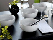 Weiße, minimalistische Keramikschalen auf dunklem Tisch mit Wassergläsern, schwarzer Vase und gefaltetem weißen Tuch; Perspektive: leicht von oben in schräger Ansicht.