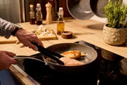 Bratpfanne mit 32 cm Durchmesser auf einem Herd, in der Hähnchenbrustfilets gebraten werden, seitliche Perspektive.