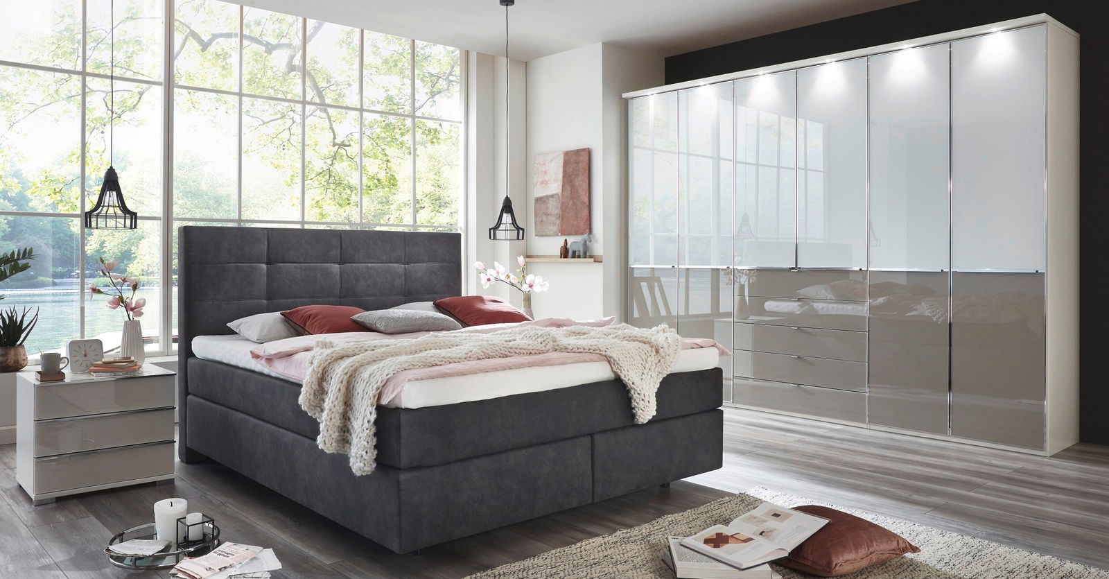 Modernes Boxspringbett in einem hellen Schlafzimmer mit großen Fenstern, seitliche Perspektive.