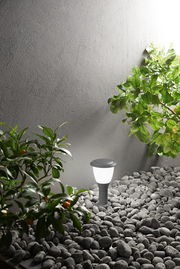 Moderne Pollerleuchte Fabas Luce THIAGO in einem Garten mit Kieselsteinen und Pflanzen, seitliche Perspektive.