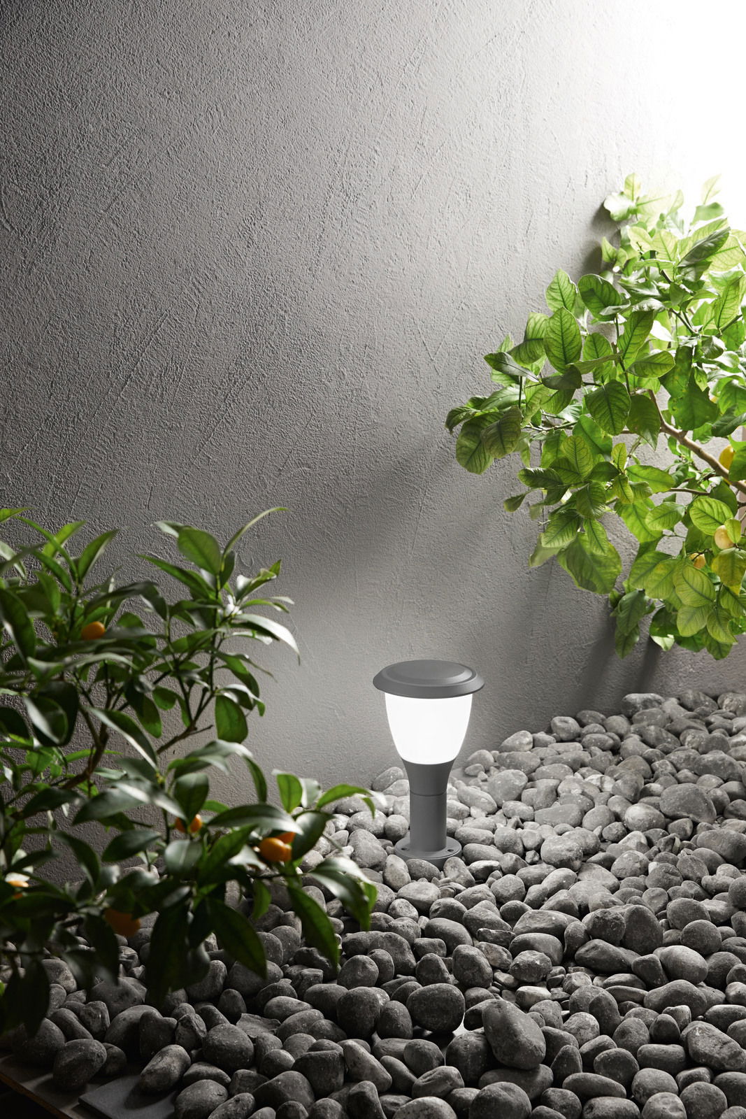 Moderne Pollerleuchte Fabas Luce THIAGO in einem Garten mit Kieselsteinen und Pflanzen, seitliche Perspektive.