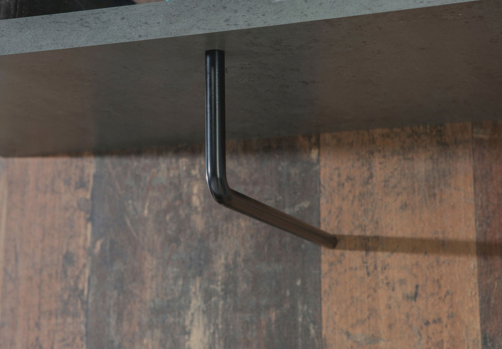 Nahaufnahme eines schwarzen Metallhakens, der an der Unterseite eines Regals befestigt ist, seitliche Perspektive.