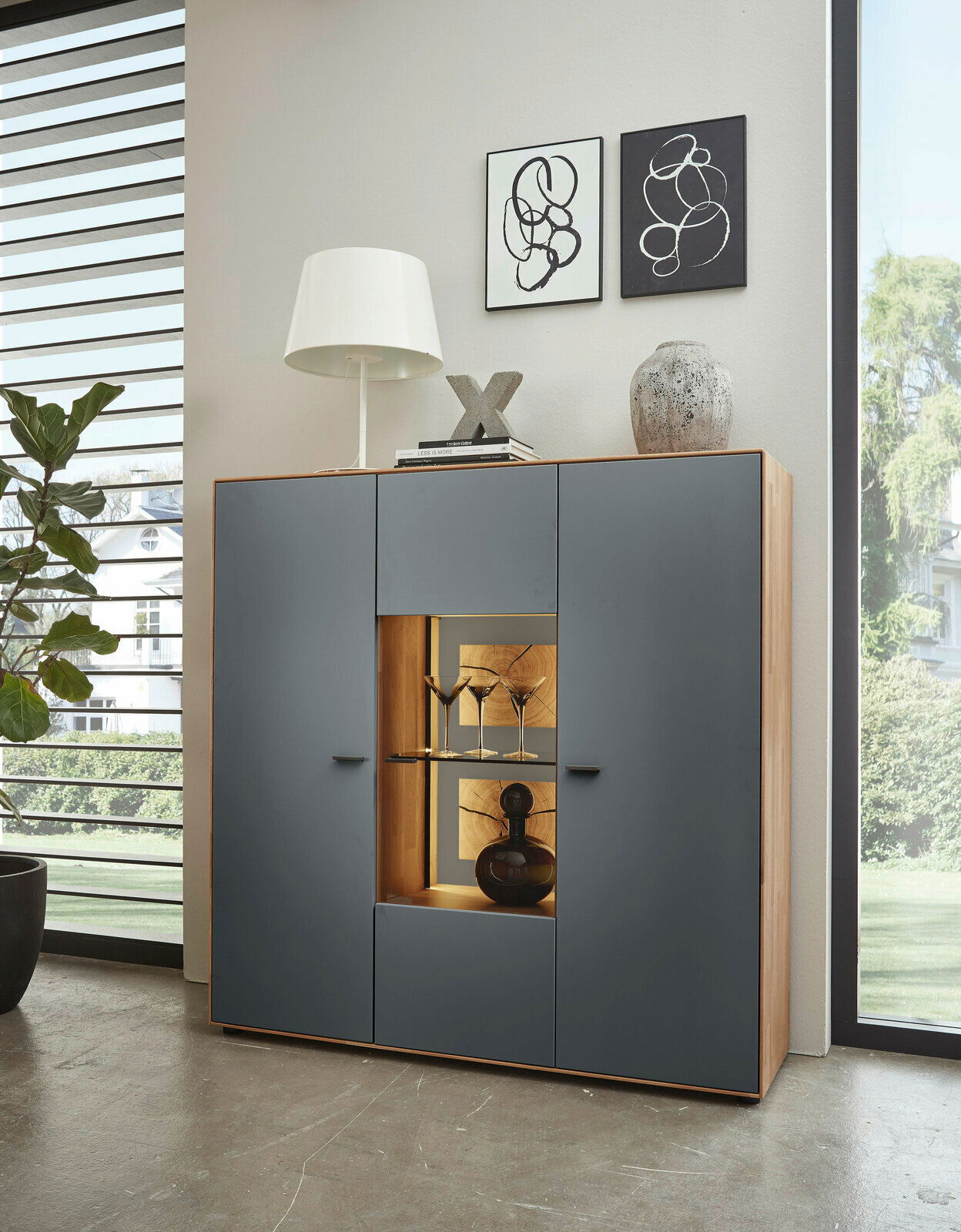 Wöstmann Markenmöbel Highboard WM 2410 Modernes Highboard mit grauen Türen und Holzrahmen, dekoriert mit einer Lampe, Büchern und Vasen, aus frontaler Perspektive.