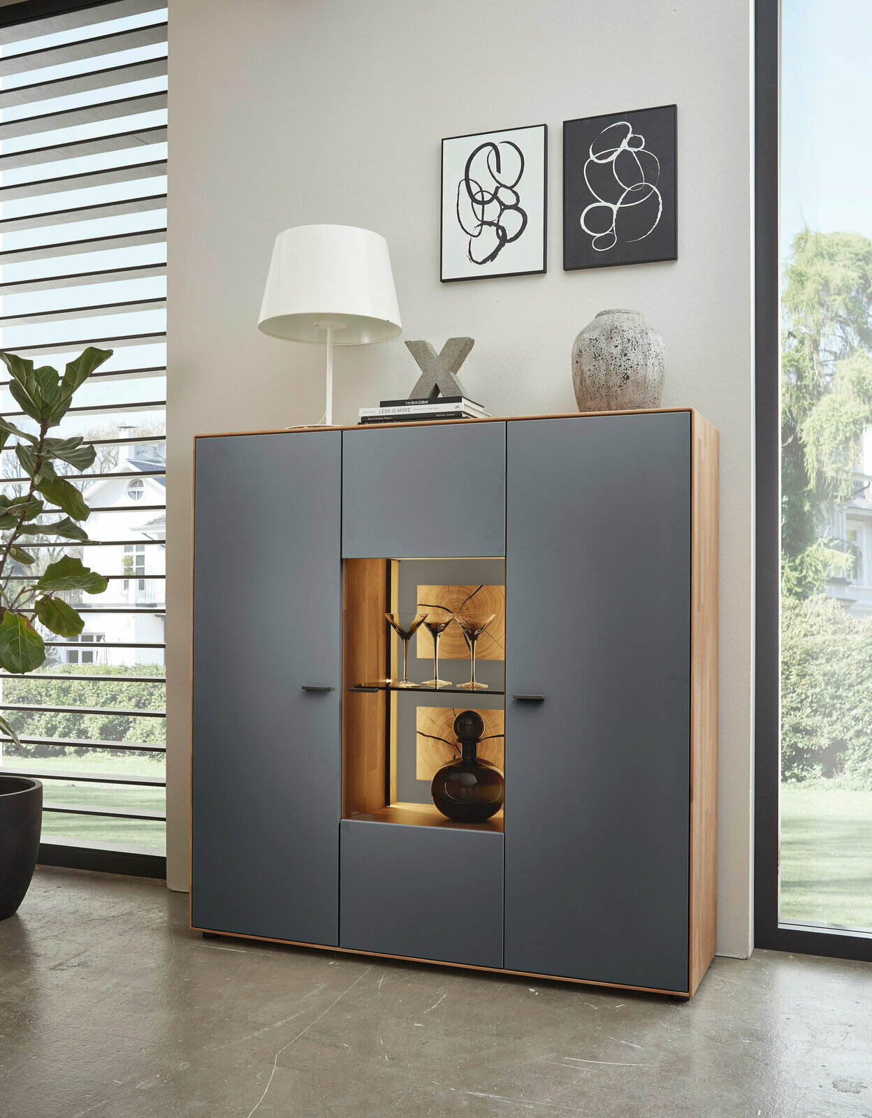 Modernes Highboard mit grauen Türen und Holzrahmen, dekoriert mit einer Lampe, Büchern und Vasen, aus frontaler Perspektive.