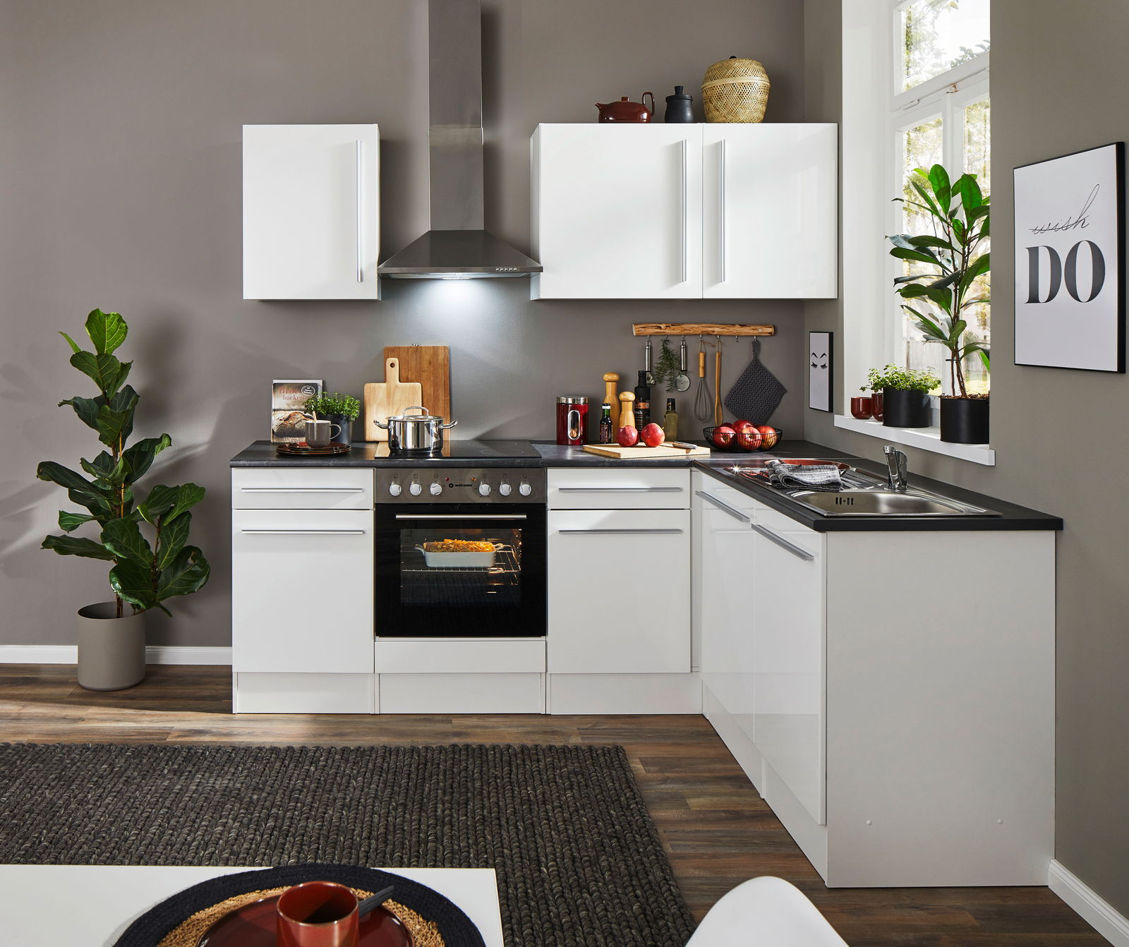 Moderne weiße Küche mit Eckunterschrank, Herd und Spüle, aus der Perspektive des Wohnzimmers betrachtet.