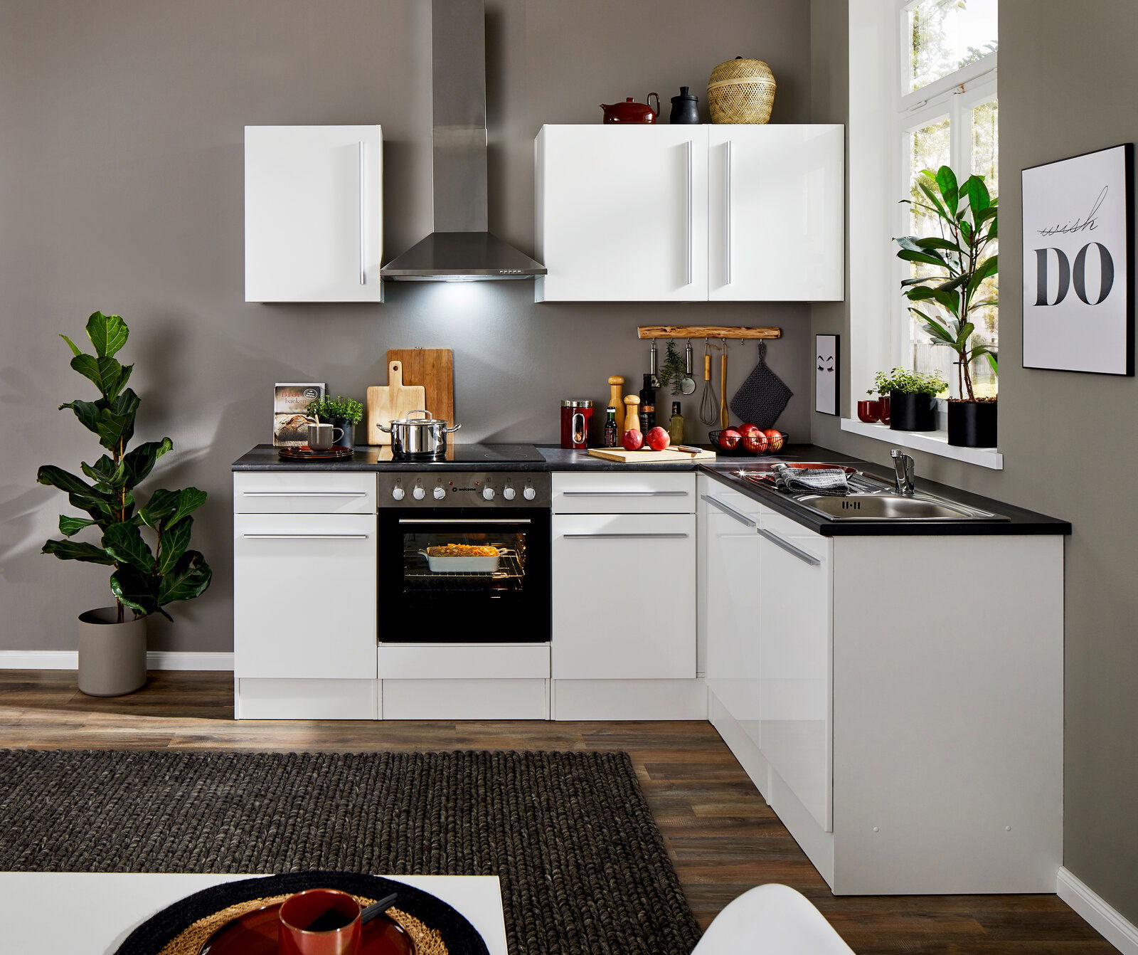 Moderne weiße Küche mit Eckunterschrank, Herd und Spüle, aus der Perspektive des Wohnzimmers betrachtet.