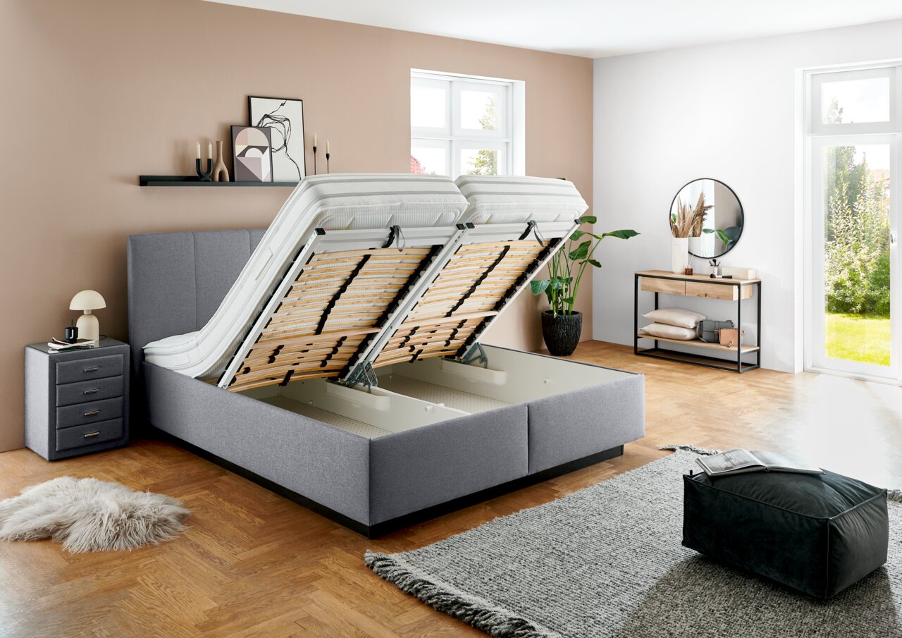 Grijs boxspringbed met omhooggeklapte lattenbodems, zijaanzicht, modern slaapkamerontwerp.