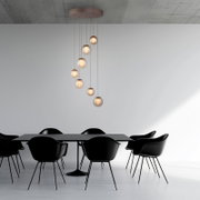 Moderne LED-Pendelleuchte mit sieben kugelförmigen Lampen, die in einer spiralförmigen Anordnung von der Decke hängen, über einem eleganten Esstisch mit schwarzen Stühlen. Perspektive: Seitenansicht.