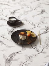 Schwarzes Tellerset Eclipse Night mit Dessert und Physalis, von oben fotografiert, auf einem Tisch mit floralem Muster.