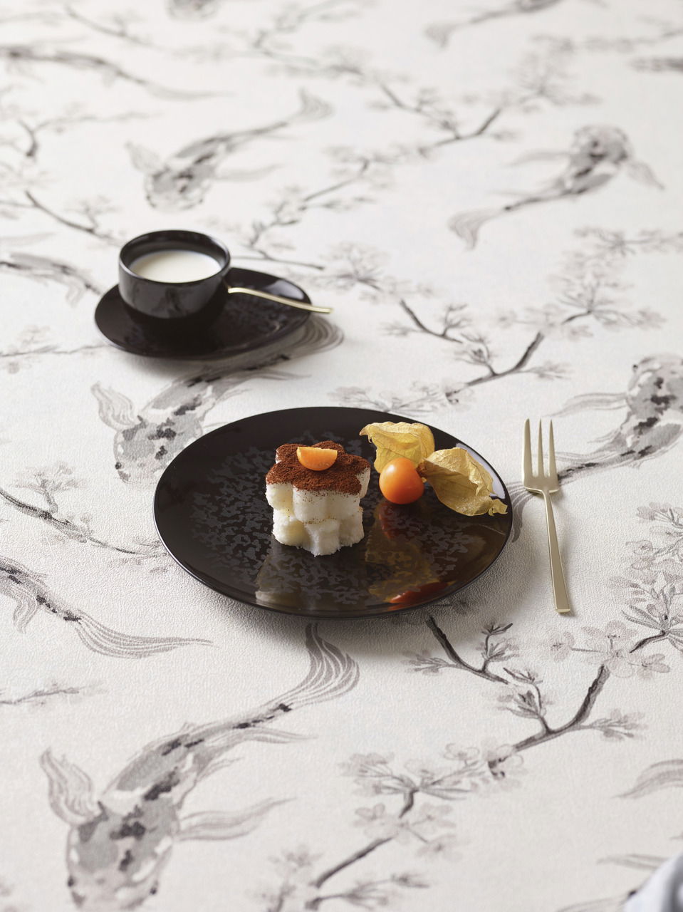 Schwarzes Tellerset Eclipse Night mit Dessert und Physalis, von oben fotografiert, auf einem Tisch mit floralem Muster.