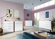 Moderne Schubkastenkommode in einem stilvoll eingerichteten Wohnzimmer mit rosa Wänden und großen Fenstern, seitliche Perspektive.