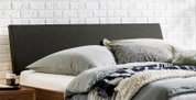 Modern bed met een donkergrijs, gestoffeerd hoofdeinde en grijs beddengoed tegen een witte bakstenen muur, zijaanzicht