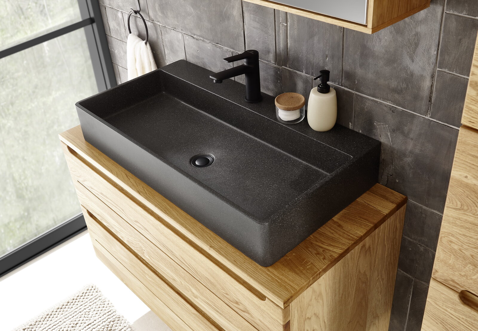 Linea Natura Terrazzo-Waschtisch ALBANY Moderner Terrazzo-Waschtisch in dunkler Farbe, von oben fotografiert, auf einem Holzunterschrank montiert, mit schwarzer Armatur und Accessoires.