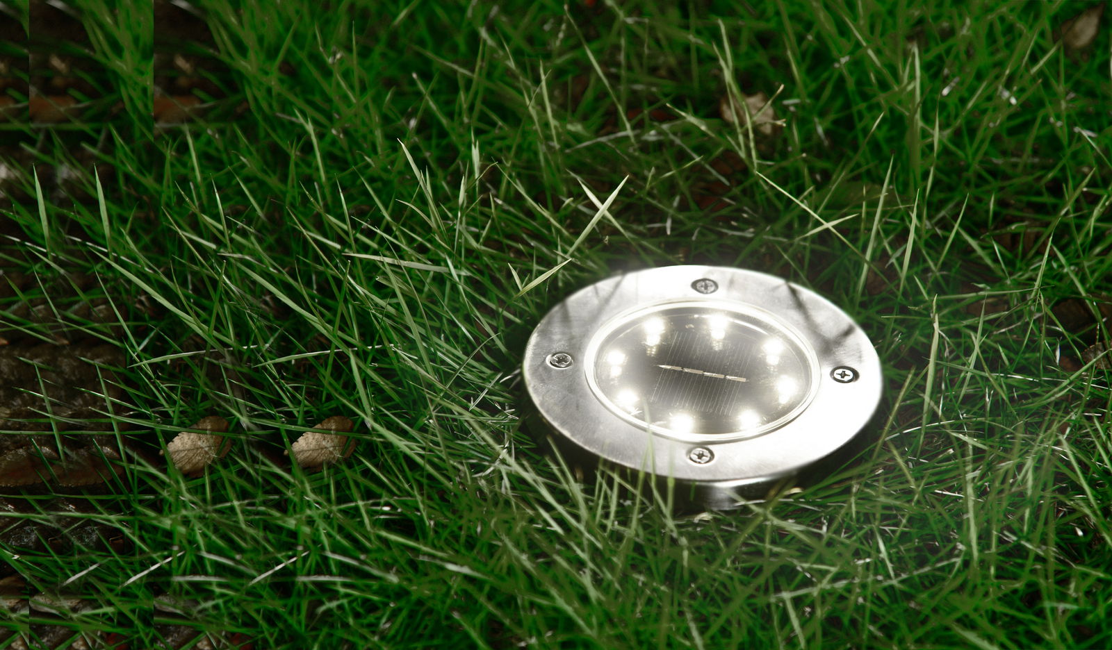 Runde Solarleuchte aus Metall, eingebettet in Gras, aus der Vogelperspektive fotografiert.