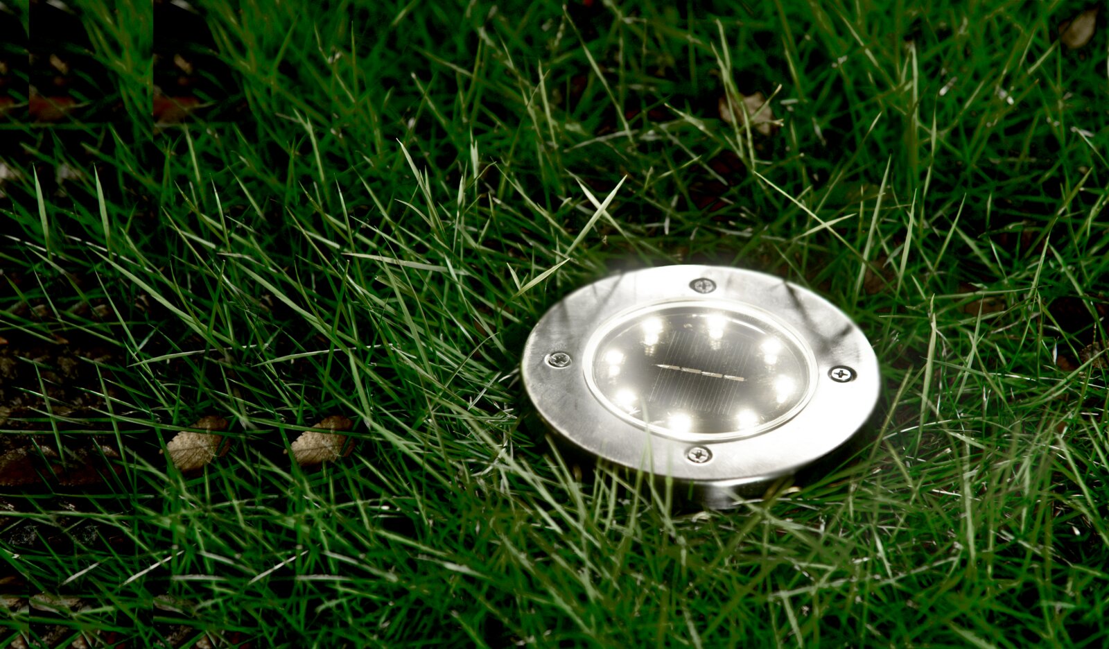 Runde Solarleuchte aus Metall, eingebettet in Gras, aus der Vogelperspektive fotografiert.