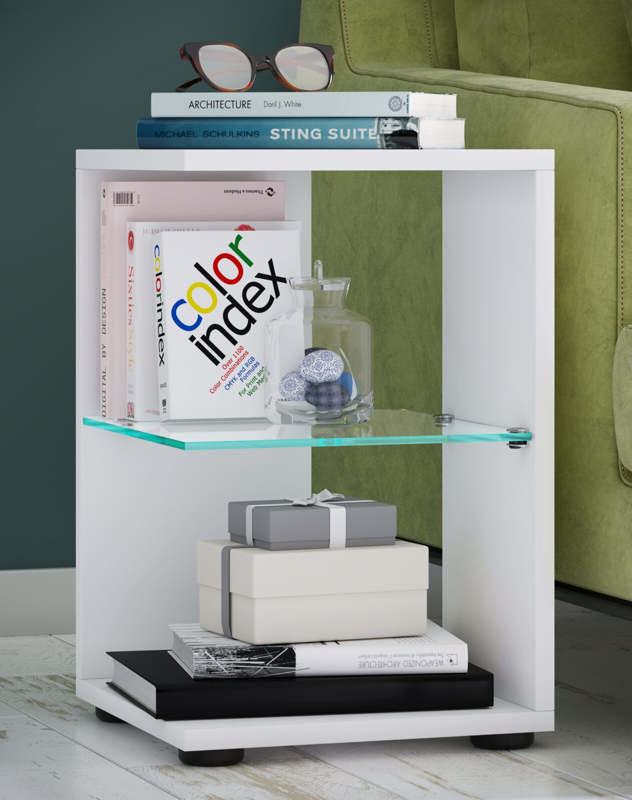 Weißes Beistellregal/Nachttisch mit Glas-Zwischenboden, bestückt mit Büchern, Deko-Glas und Geschenkboxen, neben grünem Sofa Perspektive: frontale Ansicht leicht von links.