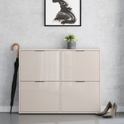 Beiges, hochglänzendes Schuhschrank-/Sideboard mit vier Klapptüren in Frontansicht, vor grauer Wand; oben steht ein kleiner Blumentopf, daneben ein Regenschirm und rechts ein Paar Pumps.