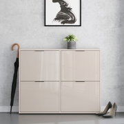 Beiges, hochglänzendes Schuhschrank-/Sideboard mit vier Klapptüren in Frontansicht, vor grauer Wand; oben steht ein kleiner Blumentopf, daneben ein Regenschirm und rechts ein Paar Pumps.