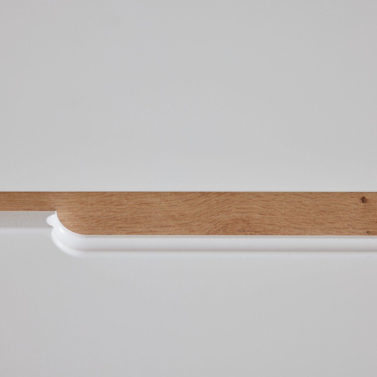 Detailansicht einer Kommode mit weißer Oberfläche und Holzleiste.